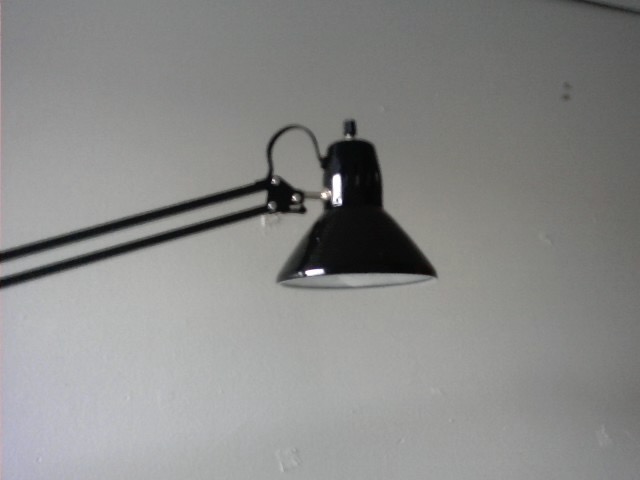 An articulating desk lamp, centered in the frame against a white wall.